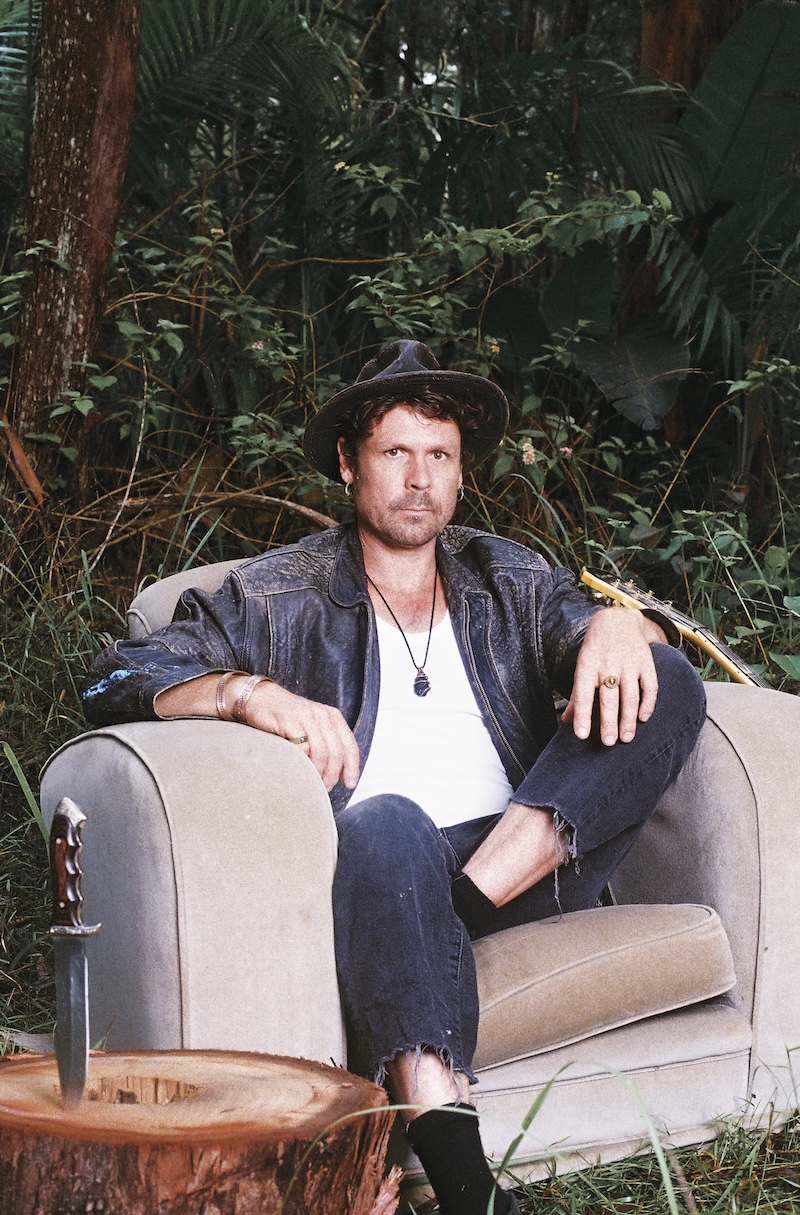 WaltSin colour portrait — looking directly at camera, seated in armchair in bush setting